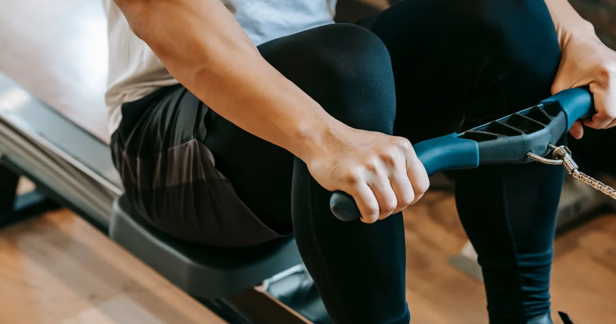 Homem fazendo remada sentada em aparelho de academia segurando o cabo com as duas mãos