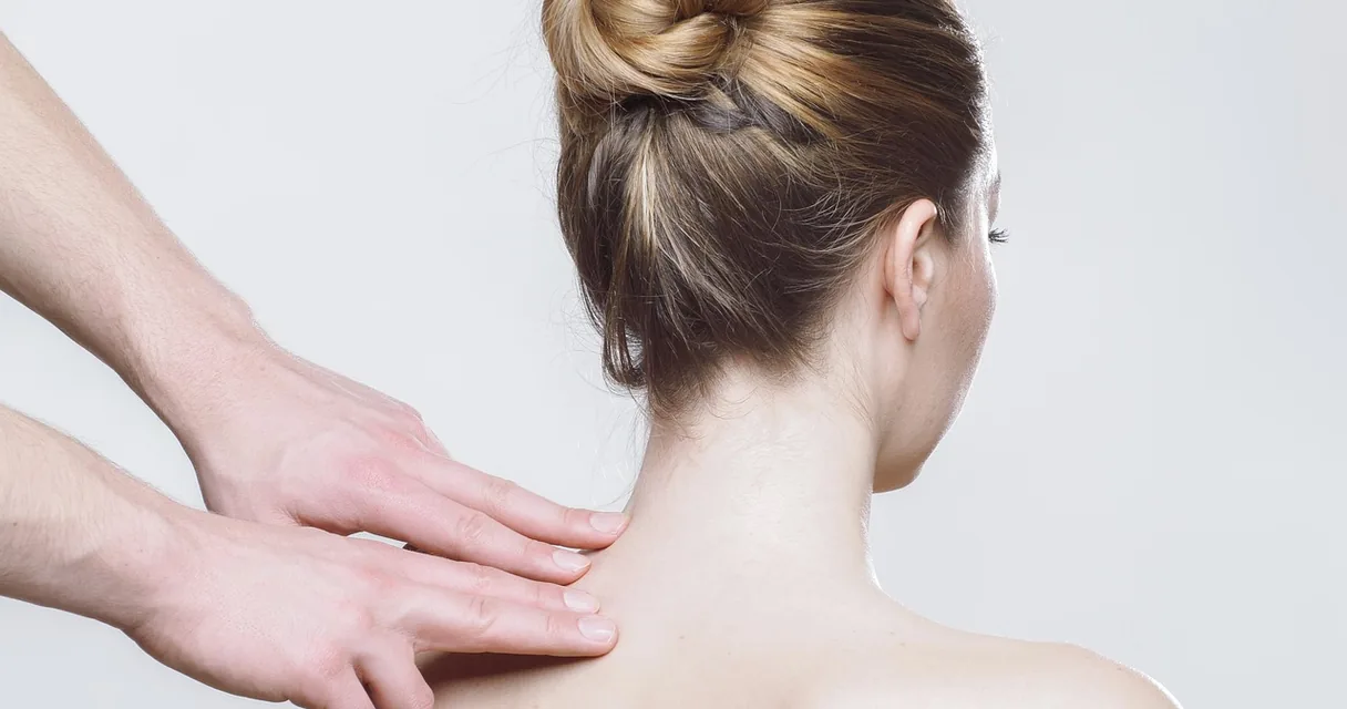 Fisioterapeuta com as mãos no ombro de uma mulher durante o atendimento